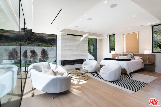 bedroom with a wall of windows, a fireplace, light hardwood / wood-style floors, and multiple windows