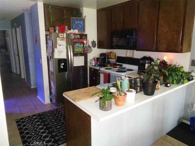 kitchen with white stove, kitchen peninsula, stainless steel refrigerator with ice dispenser, light tile patterned flooring, and dark brown cabinetry