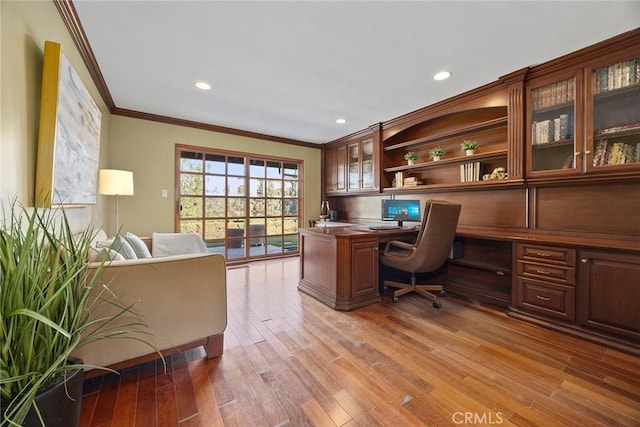 office space featuring wood-type flooring, built in desk, and crown molding