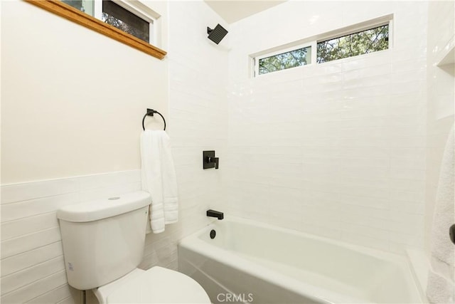 bathroom with tiled shower / bath combo, toilet, and tile walls