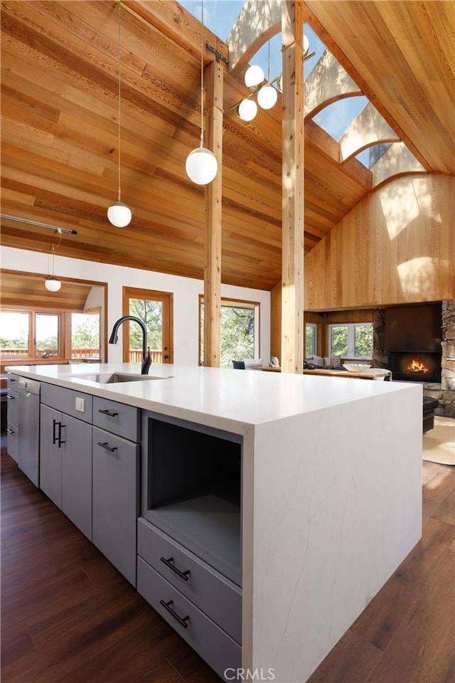 kitchen with a skylight, dishwasher, hanging light fixtures, dark hardwood / wood-style flooring, and a center island with sink