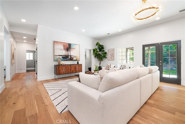 living room featuring a notable chandelier, light wood-type flooring, a wealth of natural light, and french doors