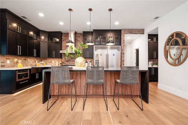 kitchen featuring stainless steel appliances, light hardwood / wood-style floors, decorative light fixtures, decorative backsplash, and a kitchen island