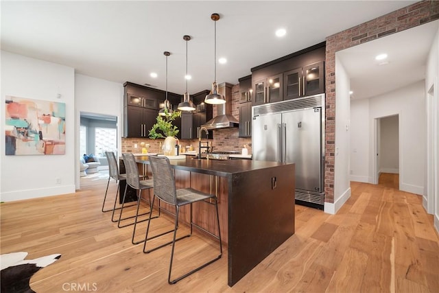 kitchen with decorative backsplash, pendant lighting, light hardwood / wood-style floors, built in refrigerator, and an island with sink