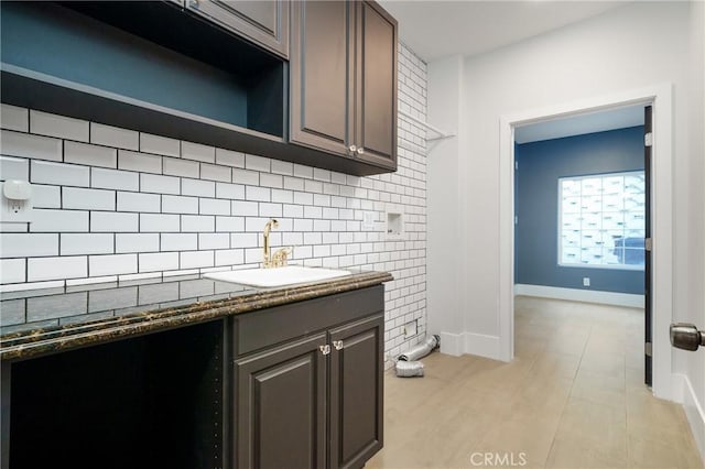 kitchen with tasteful backsplash, dark brown cabinetry, sink, dark stone countertops, and light tile patterned flooring