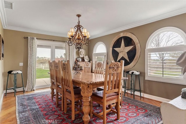 dining area with a notable chandelier, ornamental molding, and light hardwood / wood-style flooring