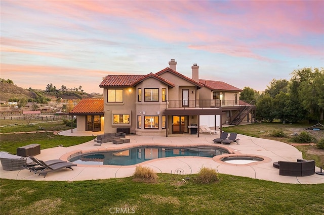 back house at dusk featuring a pool with hot tub, a yard, and a patio