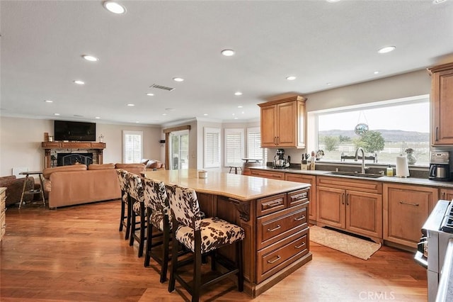 kitchen featuring light hardwood / wood-style floors, a center island, a kitchen breakfast bar, crown molding, and sink