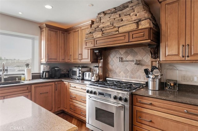 kitchen featuring custom exhaust hood, stainless steel range, dark stone countertops, decorative backsplash, and sink