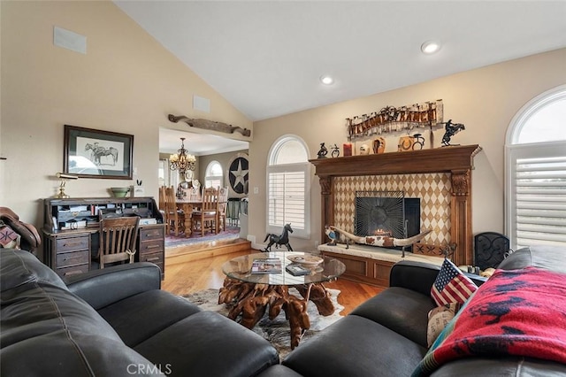 living room with high vaulted ceiling, a tile fireplace, an inviting chandelier, and light hardwood / wood-style flooring