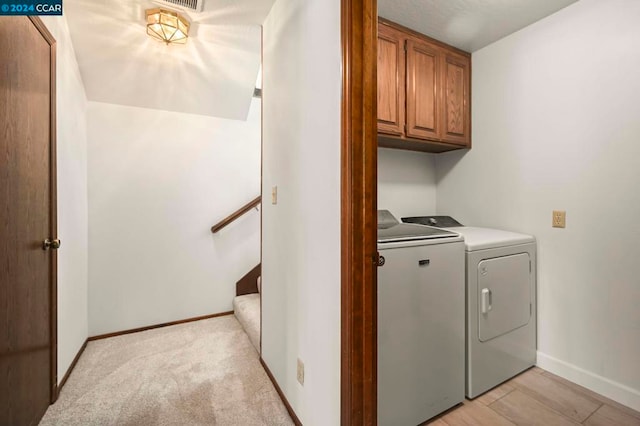 clothes washing area featuring cabinets, light carpet, and washer and dryer