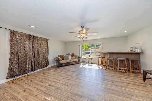 sitting room with light hardwood / wood-style floors, ceiling fan, and indoor bar