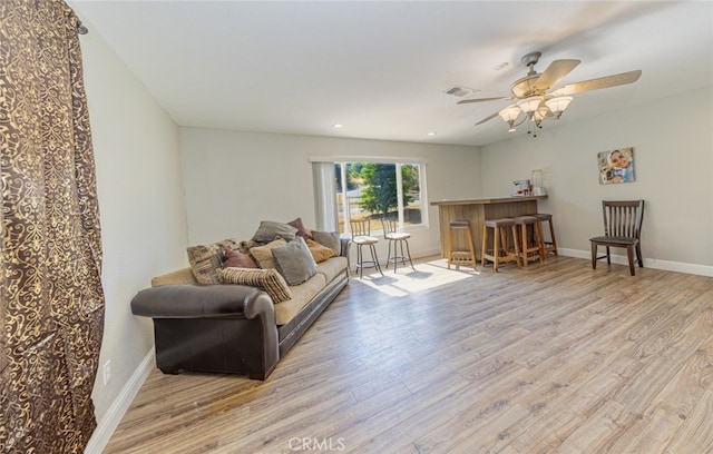 living room with bar area, ceiling fan, and light hardwood / wood-style flooring