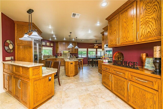 kitchen featuring a kitchen bar, hanging light fixtures, appliances with stainless steel finishes, an island with sink, and light stone countertops