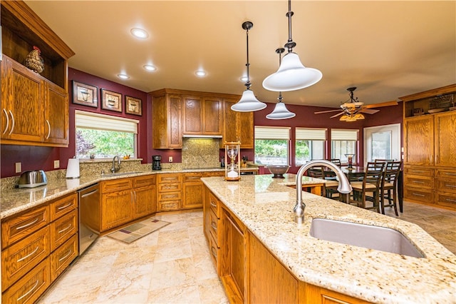 kitchen featuring light stone counters, stainless steel dishwasher, sink, and hanging light fixtures