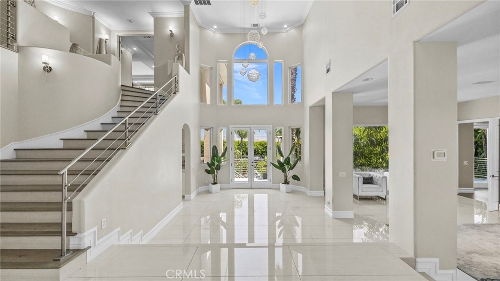 foyer entrance featuring a towering ceiling, ornamental molding, and french doors