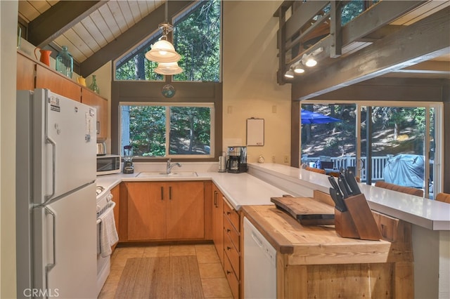 kitchen with sink, kitchen peninsula, vaulted ceiling with beams, white appliances, and decorative light fixtures