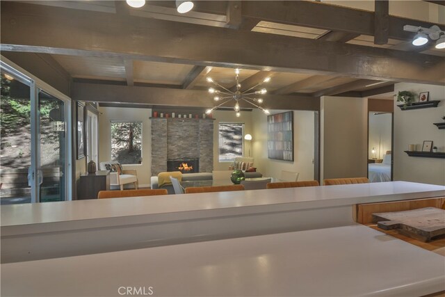 kitchen featuring beam ceiling, a chandelier, and a stone fireplace