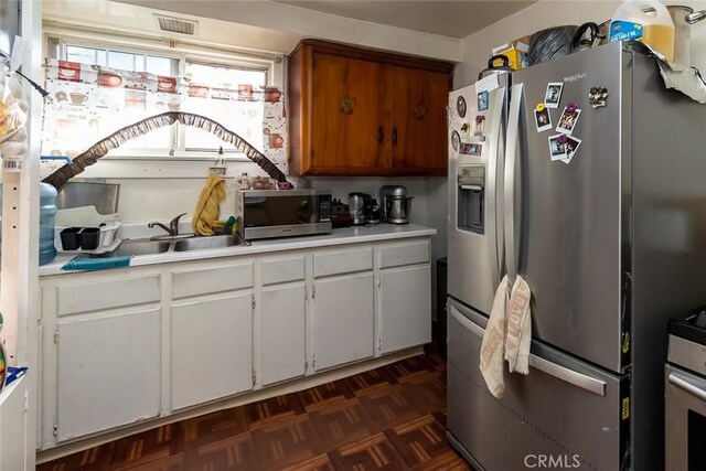 kitchen featuring stainless steel appliances, white cabinets, sink, and dark parquet flooring