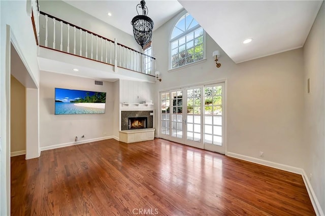 unfurnished living room featuring french doors, a towering ceiling, a tile fireplace, hardwood / wood-style flooring, and a notable chandelier