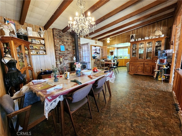 dining space with a wood stove, beam ceiling, wood walls, and a chandelier