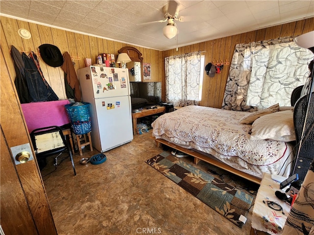 bedroom featuring wooden walls, ceiling fan, and white fridge