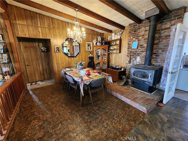 dining space featuring an inviting chandelier, beamed ceiling, wood walls, and a wood stove