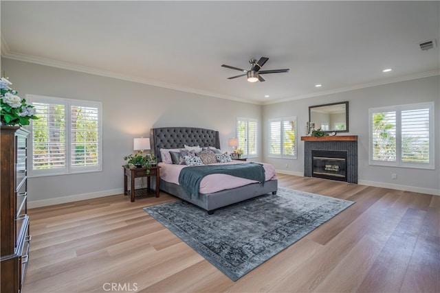 bedroom with a tiled fireplace, light hardwood / wood-style flooring, ornamental molding, and ceiling fan