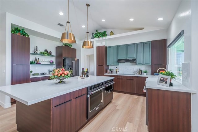 kitchen featuring light hardwood / wood-style flooring, appliances with stainless steel finishes, hanging light fixtures, a kitchen island, and vaulted ceiling