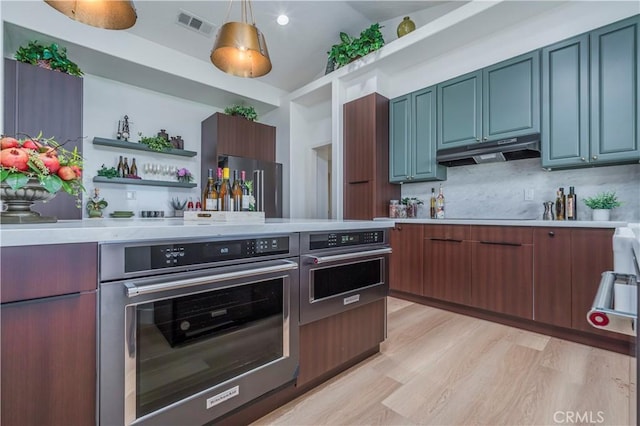 kitchen featuring lofted ceiling, decorative backsplash, hanging light fixtures, stainless steel oven, and light hardwood / wood-style flooring