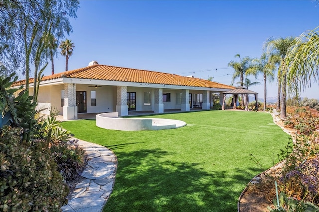 rear view of property with ceiling fan and a yard