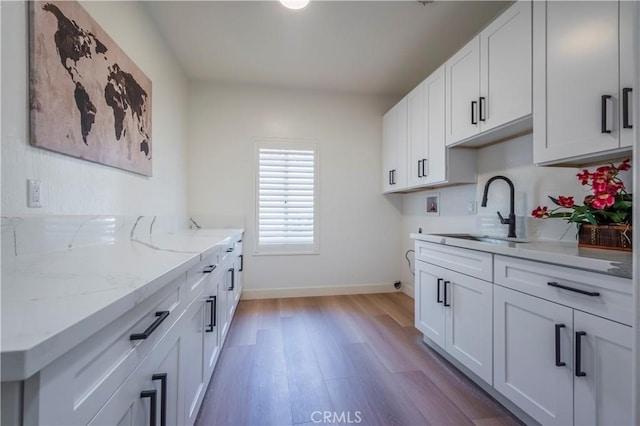 kitchen with sink, white cabinets, light stone counters, and light wood-type flooring