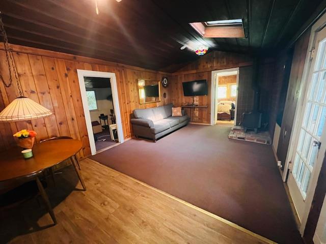 living room featuring hardwood / wood-style flooring, lofted ceiling with skylight, and wooden walls