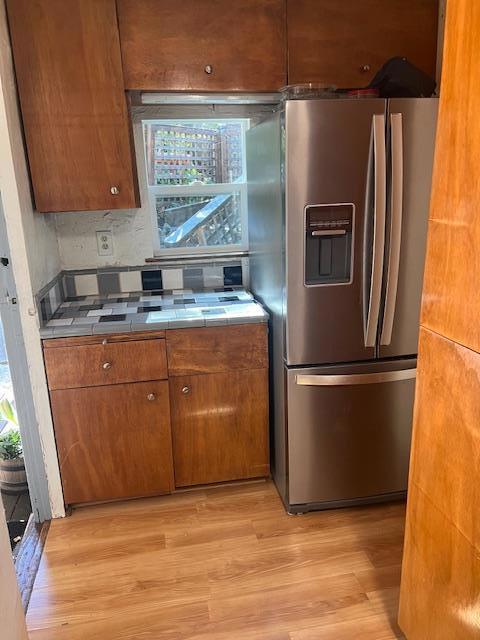 kitchen with tasteful backsplash, stainless steel refrigerator with ice dispenser, tile countertops, and light hardwood / wood-style flooring