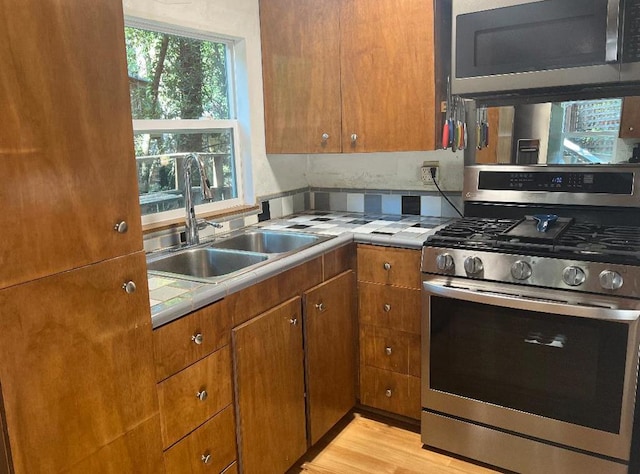 kitchen with tile counters, sink, light wood-type flooring, and appliances with stainless steel finishes