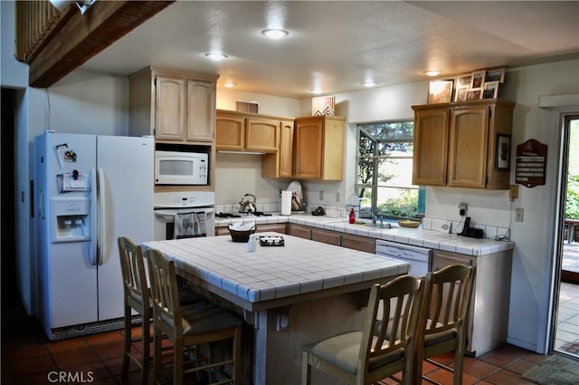 kitchen featuring dark tile patterned flooring, a kitchen breakfast bar, tile counters, and white appliances