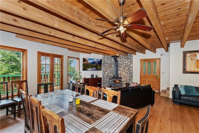 dining space featuring light hardwood / wood-style floors, beam ceiling, wood ceiling, a wood stove, and french doors