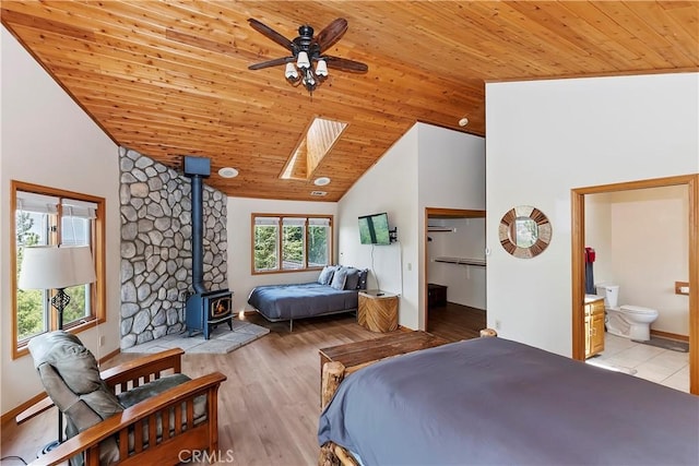 bedroom featuring ensuite bathroom, vaulted ceiling with skylight, a wood stove, a walk in closet, and wooden ceiling