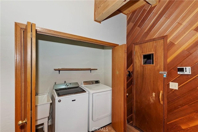 clothes washing area with sink, independent washer and dryer, and wooden walls