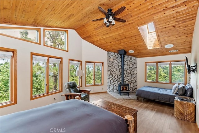 bedroom featuring ceiling fan, wood ceiling, a wood stove, and light hardwood / wood-style floors