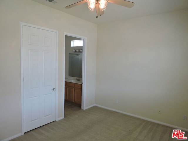 unfurnished bedroom featuring ensuite bathroom, light colored carpet, sink, and ceiling fan