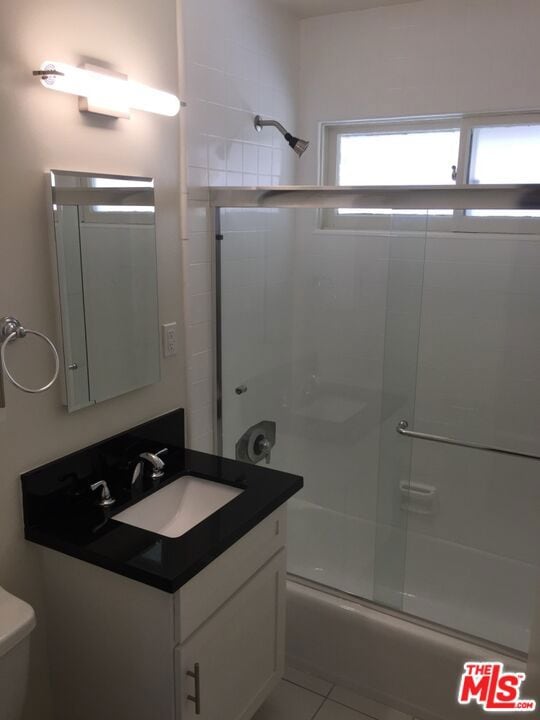 full bathroom featuring tile patterned flooring, vanity, combined bath / shower with glass door, and toilet