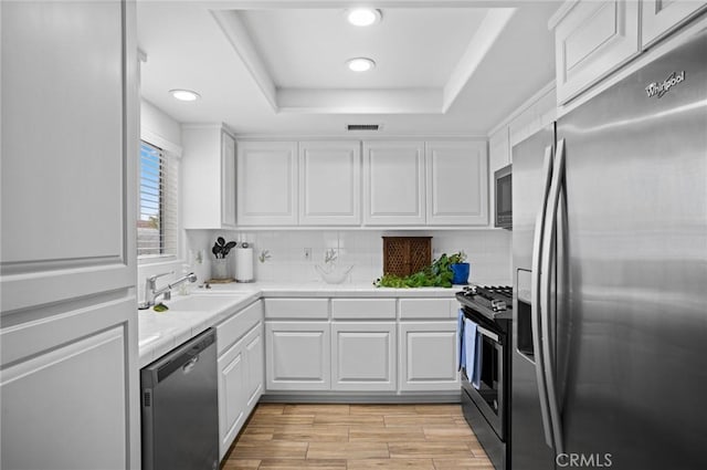 kitchen with appliances with stainless steel finishes, a raised ceiling, sink, light hardwood / wood-style flooring, and white cabinets