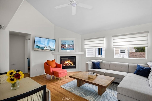 living room with a wealth of natural light, ceiling fan, wood-type flooring, and vaulted ceiling