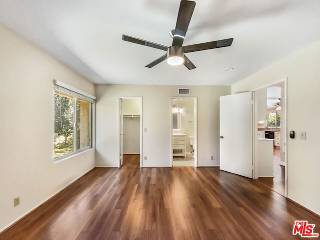 unfurnished bedroom featuring ensuite bath, ceiling fan, a spacious closet, dark hardwood / wood-style flooring, and a closet