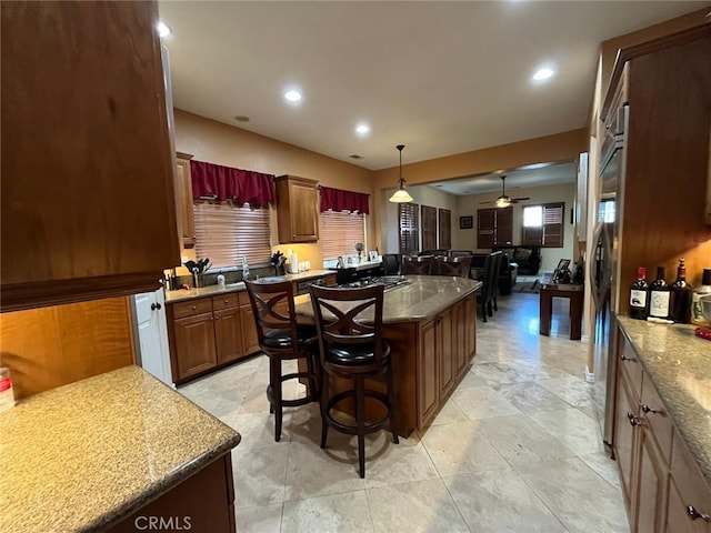 kitchen with a center island, a kitchen bar, hanging light fixtures, ceiling fan, and stone countertops