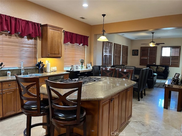 kitchen featuring ceiling fan, hanging light fixtures, sink, stainless steel gas stovetop, and a center island