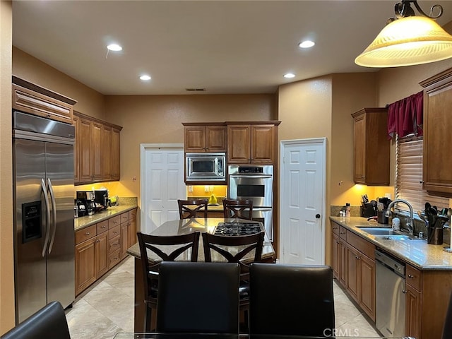 kitchen with light tile patterned flooring, built in appliances, sink, decorative light fixtures, and light stone countertops