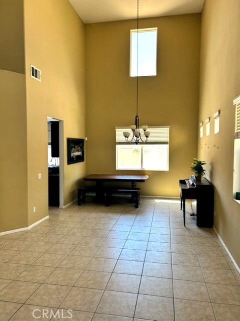 unfurnished living room with a towering ceiling, light tile patterned flooring, plenty of natural light, and an inviting chandelier