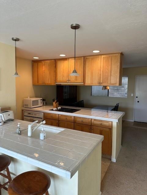 kitchen featuring decorative light fixtures, a breakfast bar, tile countertops, and black electric cooktop